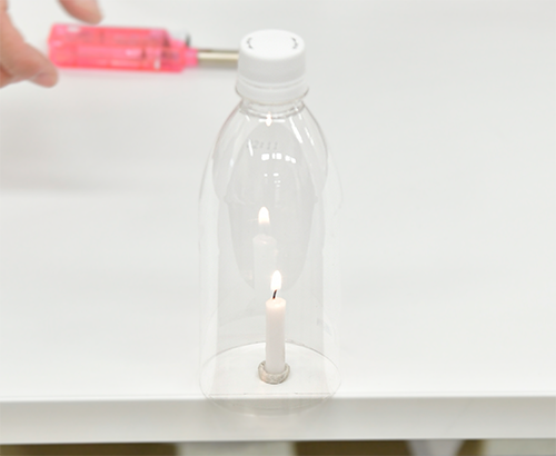 蓋をして底が開いてるペットボトルを火のついたろうそくにかぶせている写真