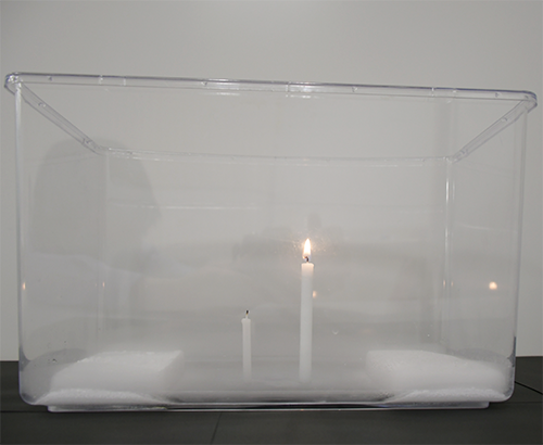 水槽の中にドライアイス、火のついた大きいろうそく、火が消えた小さいろうそくがある写真